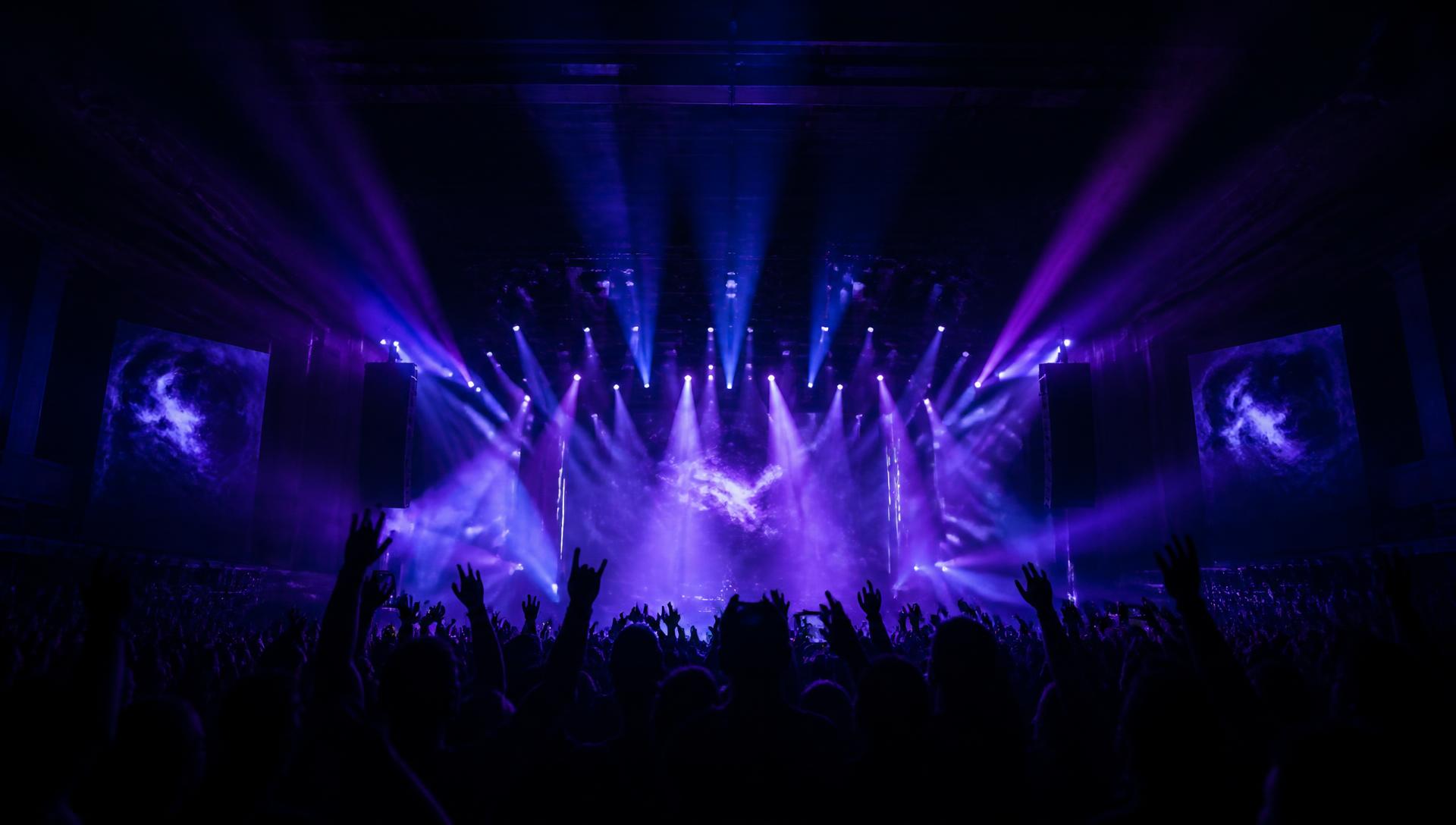 Violet and blue stage lights sweeping over a packed concert crowd at a modern Atlanta music venue